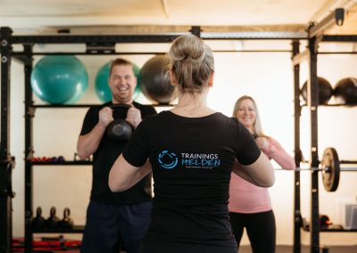 Trainerin von hinten mit 2 Kunden mit Kettlebell