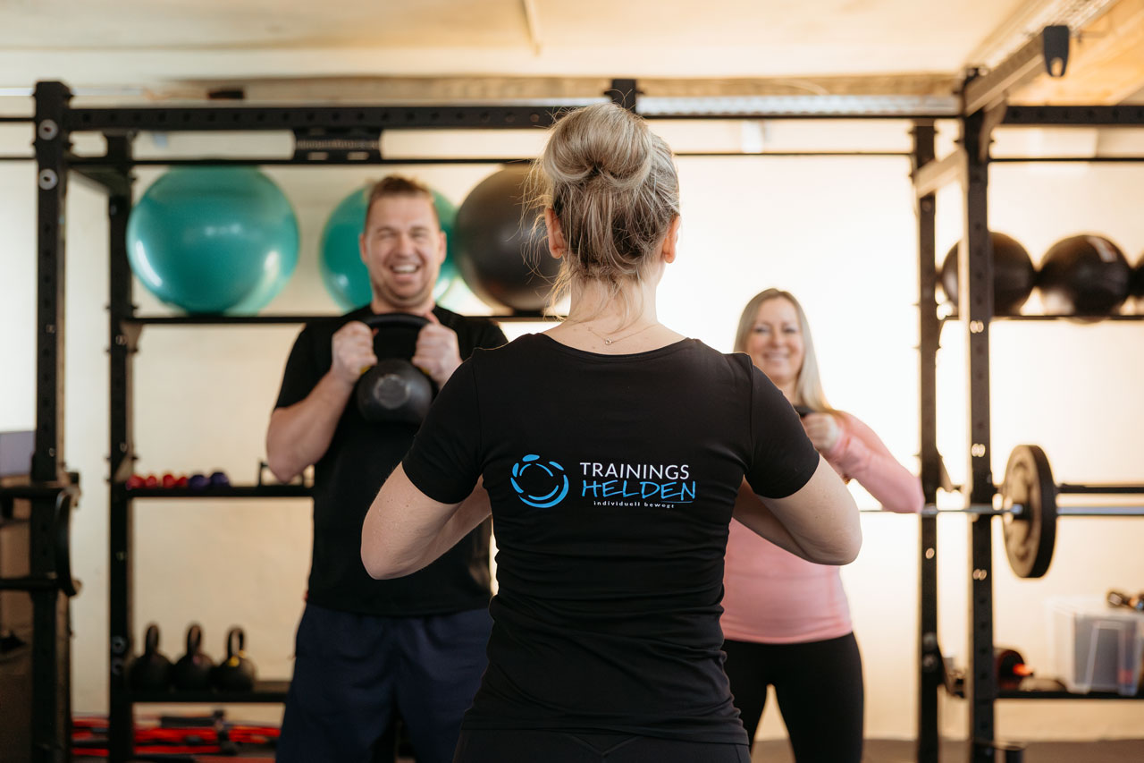 Trainerin von hinten mit 2 Kunden mit Kettlebell